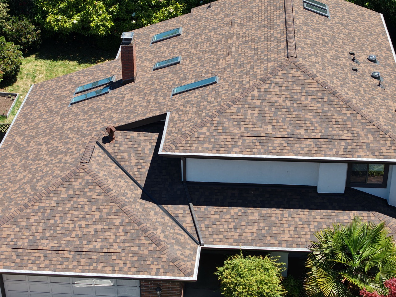 Aerial view of a brown designer shingle roof with skylights and a brick chimney.