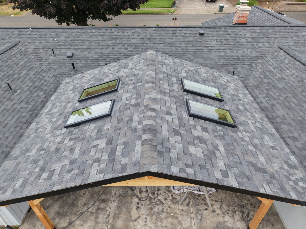 Top-down view of a new gray shingle roof with four black-framed skylights.